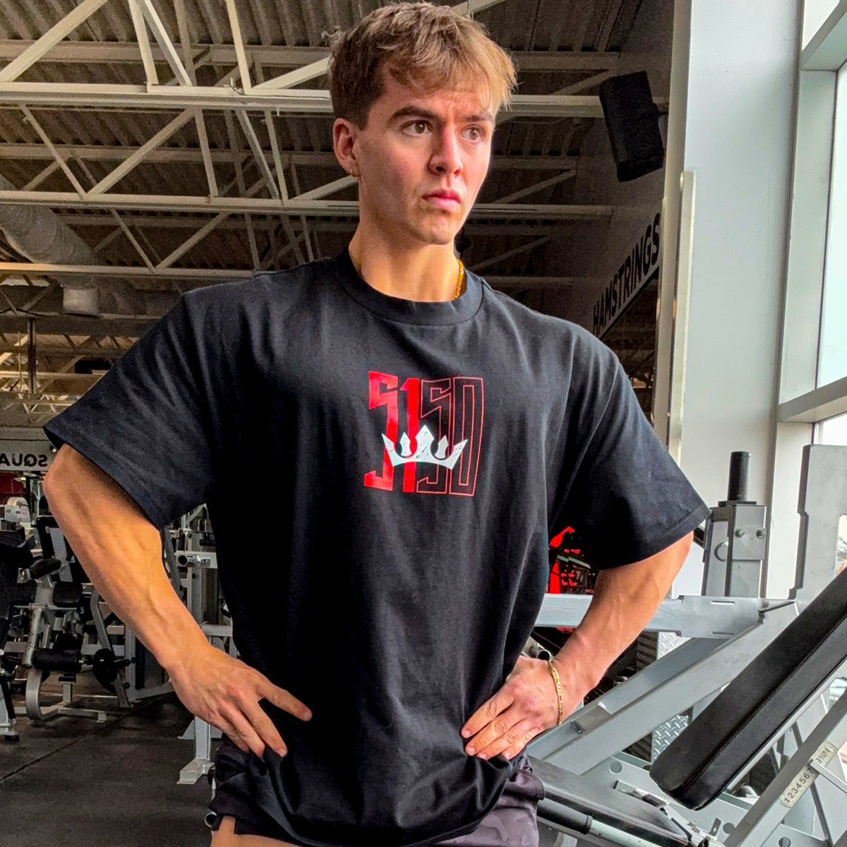 Man in gym wearing black 5% Nutrition t-shirt with red logo and camo shorts, hands on hips